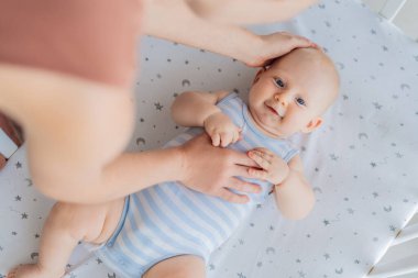 Anne beşikte oturup bebeğini nazikçe okşuyor evdeki rahat bir yatakta yatıyor. Sevgi, güven ve sükunetle dolu sıcak ve samimi bir an. Annelik, bebek rahatlığı ve duygusal bağ konsepti..