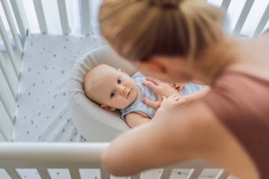 Anne beşikte nazikçe oturuyor ve sıcak bir koza yuvasında bebeğini okşuyor. Evde şefkatli samimi bir ilgi ve güven anı. Annelik, bebek uykusu ve duygusal bağ konsepti..