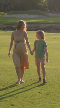 Hamile anne ve büyük oğlu gün batımında yemyeşil bir alanda neşeli anların tadını çıkarıyorlar. Güzel annelik bağı, çocukluk sevinci ve sevgi dolu aile zamanı. Açık havada mutluluk