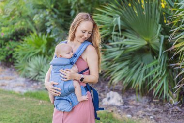 Bir anne, ergonomik bir bebek taşıyıcısı ile bebeğini vücuduna yakın bir şekilde dışarı çıkar. Bebek giyimi, aktif ebeveynlik, rahatlık, bağlılık, hareketlilik ve modern aile yaşam tarzı kavramı