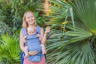 Bir anne, ergonomik bir bebek taşıyıcısı ile bebeğini vücuduna yakın bir şekilde dışarı çıkar. Bebek giyimi, aktif ebeveynlik, rahatlık, bağlılık, hareketlilik ve modern aile yaşam tarzı kavramı