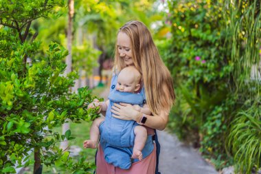 Bir anne, ergonomik bir bebek taşıyıcısı ile bebeğini vücuduna yakın bir şekilde dışarı çıkar. Bebek giyimi, aktif ebeveynlik, rahatlık, bağlılık, hareketlilik ve modern aile yaşam tarzı kavramı