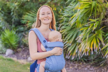 Bir anne, ergonomik bir bebek taşıyıcısı ile bebeğini vücuduna yakın bir şekilde dışarı çıkar. Bebek giyimi, aktif ebeveynlik, rahatlık, bağlılık, hareketlilik ve modern aile yaşam tarzı kavramı