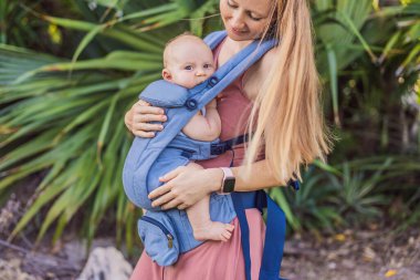 Bir anne, ergonomik bir bebek taşıyıcısı ile bebeğini vücuduna yakın bir şekilde dışarı çıkar. Bebek giyimi, aktif ebeveynlik, rahatlık, bağlılık, hareketlilik ve modern aile yaşam tarzı kavramı