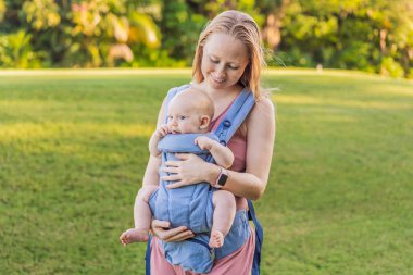 Bir anne, ergonomik bir bebek taşıyıcısı ile bebeğini vücuduna yakın bir şekilde dışarı çıkar. Bebek giyimi, aktif ebeveynlik, rahatlık, bağlılık, hareketlilik ve modern aile yaşam tarzı kavramı
