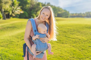 Bir anne, ergonomik bir bebek taşıyıcısı ile bebeğini vücuduna yakın bir şekilde dışarı çıkar. Bebek giyimi, aktif ebeveynlik, rahatlık, bağlılık, hareketlilik ve modern aile yaşam tarzı kavramı
