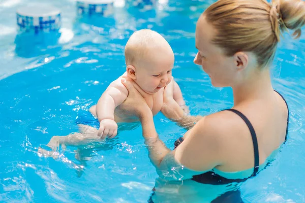 Anne bebeğini yüzme havuzunda yıkıyor, su saatinde bebeği kucağında tutuyor ve ona bakıyor. Şefkatli bir bağ kurma anı güven ve özeni gösterir. Bebek yüzme, erken gelişim ve sağlıklı annelik.