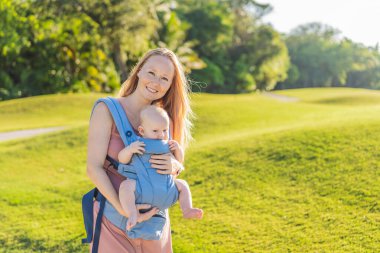 Bir anne, ergonomik bir bebek taşıyıcısı ile bebeğini vücuduna yakın bir şekilde dışarı çıkar. Bebek giyimi, aktif ebeveynlik, rahatlık, bağlılık, hareketlilik ve modern aile yaşam tarzı kavramı