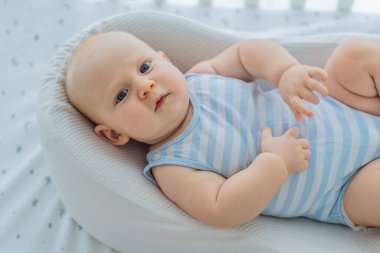 Bebek, bir beşiğin içindeki sıcak bir kozada huzur içinde uzanıyor. Evde kendini güvende ve sakin hissediyor. Yumuşak ışık ve ılık atmosfer rahatlık ve ilgiyi vurgular. Bebek uykusu, güvenlik ve nazik ebeveynlik kavramı.