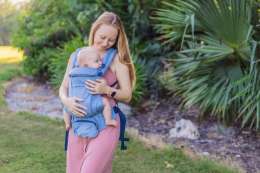 Bir anne, ergonomik bir bebek taşıyıcısı ile bebeğini vücuduna yakın bir şekilde dışarı çıkar. Bebek giyimi, aktif ebeveynlik, rahatlık, bağlılık, hareketlilik ve modern aile yaşam tarzı kavramı