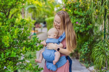 Bir anne, ergonomik bir bebek taşıyıcısı ile bebeğini vücuduna yakın bir şekilde dışarı çıkar. Bebek giyimi, aktif ebeveynlik, rahatlık, bağlılık, hareketlilik ve modern aile yaşam tarzı kavramı