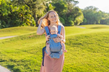 Bir anne, ergonomik bir bebek taşıyıcısı ile bebeğini vücuduna yakın bir şekilde dışarı çıkar. Bebek giyimi, aktif ebeveynlik, rahatlık, bağlılık, hareketlilik ve modern aile yaşam tarzı kavramı