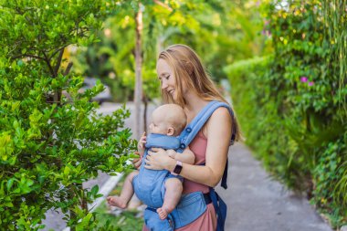 Bir anne, ergonomik bir bebek taşıyıcısı ile bebeğini vücuduna yakın bir şekilde dışarı çıkar. Bebek giyimi, aktif ebeveynlik, rahatlık, bağlılık, hareketlilik ve modern aile yaşam tarzı kavramı
