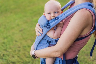 Bir anne, ergonomik bir bebek taşıyıcısı ile bebeğini vücuduna yakın bir şekilde dışarı çıkar. Bebek giyimi, aktif ebeveynlik, rahatlık, bağlılık, hareketlilik ve modern aile yaşam tarzı kavramı
