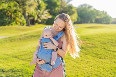 Bir anne, ergonomik bir bebek taşıyıcısı ile bebeğini vücuduna yakın bir şekilde dışarı çıkar. Bebek giyimi, aktif ebeveynlik, rahatlık, bağlılık, hareketlilik ve modern aile yaşam tarzı kavramı