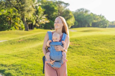 Bir anne, ergonomik bir bebek taşıyıcısı ile bebeğini vücuduna yakın bir şekilde dışarı çıkar. Bebek giyimi, aktif ebeveynlik, rahatlık, bağlılık, hareketlilik ve modern aile yaşam tarzı kavramı