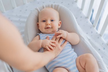 Anne beşikte nazikçe oturuyor ve sıcak bir koza yuvasında bebeğini okşuyor. Evde şefkatli samimi bir ilgi ve güven anı. Annelik, bebek uykusu ve duygusal bağ konsepti..