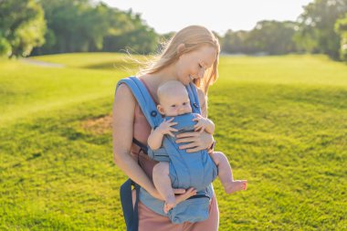 Bir anne, ergonomik bir bebek taşıyıcısı ile bebeğini vücuduna yakın bir şekilde dışarı çıkar. Bebek giyimi, aktif ebeveynlik, rahatlık, bağlılık, hareketlilik ve modern aile yaşam tarzı kavramı
