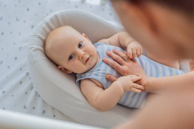 Anne beşikte nazikçe oturuyor ve sıcak bir koza yuvasında bebeğini okşuyor. Evde şefkatli samimi bir ilgi ve güven anı. Annelik, bebek uykusu ve duygusal bağ konsepti..