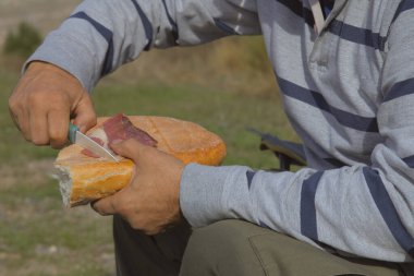 Beyaz gömlekli ve siyah şapkalı bir adam sandviç tutuyor.