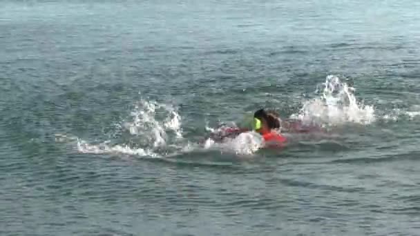 Boy Dressed in Red Shorts and Orange Inflatable Sleeves is Swimming and Splashing in Sea — Stock Video