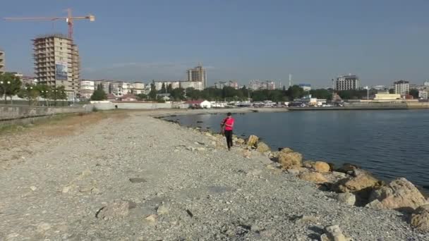 핑크 탑 입은 여자 여름에서 화창한 날씨에 해변에 걷고 있다 — 비디오