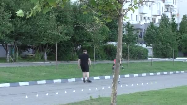Два підлітки є Роликові ковзани в парку у літніх канікул, сонячний день в тіні дерев — стокове відео