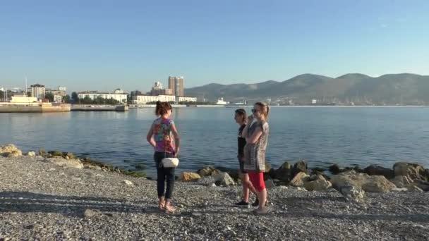 Τρεις γυναίκες στέκονται στην παραλία με βότσαλα σε φόντο της ακτογραμμής και αστικό τοπίο στην ηλιόλουστη μέρα του καλοκαιριού Βίντεο Κλιπ