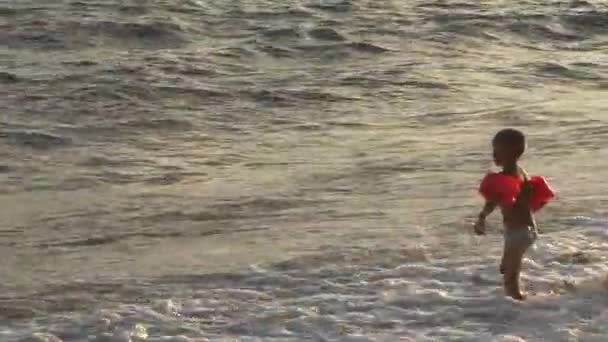 Dos niños juegan con grandes olas en la playa del mar en la noche caliente en las vacaciones de verano — Vídeo de stock