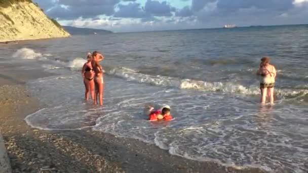 Ženy v plavkách stojí na pobřeží moře, chlapec hraje v mořských vln — Stock video