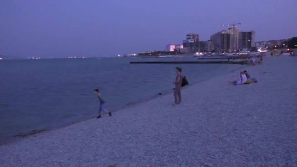 Люди на галькового пляжу моря в сутінках час — стокове відео