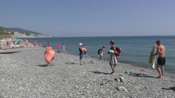 Pohled na stojící lidi v oblázkové pláže v blízkosti moře a bílé skály na pozadí ve slunečný den — Stock video