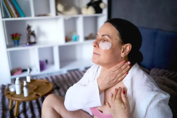        Yatakta iç çamaşırlı yaşlı bir kadın vücut kozmetikleriyle rutin bir kişisel bakım yapıyor.                        