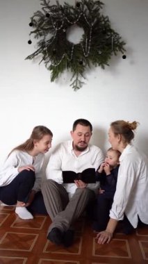 Noel kutlaması sırasında İncil okuyan çocuklu bir aile.