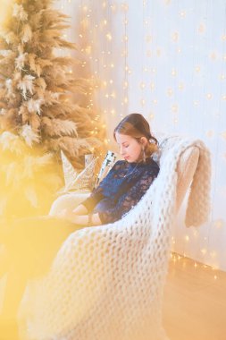 Alışılmadık bir Noel ağacının yanında, altın ışıklarla çevrili elbise giymiş genç bir kız.