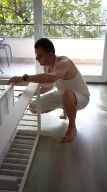 Yeni baba, yeni bebeği için parlak, basit bir odada beşik yapacak.