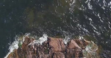 Güneşli yaz mevsiminde kayalık sahile vuran dalgaların aşağı yönlü hava görüntüsü, Pirttisaari doğa rezervi, Pirttisaari, Porvoo, Finlandiya.