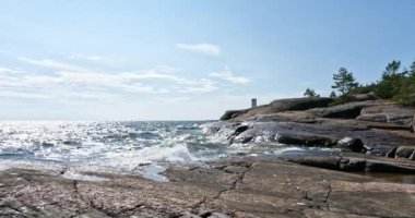 Pirttisaari doğa kayalık deniz manzarası güneşli yaz havasında kıyıya vuran dalgalarla gökyüzünde bulutlar, Pirttisaari, Porvoo, Finlandiya. 