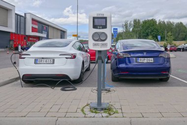 Laajalahti, Finlandiya - 19 Ağustos. 2025: Beyaz ve mavi Tesla Model 3 elektrikli araba alışveriş merkezinin park yerine park edildi elektrik şarj istasyonu.