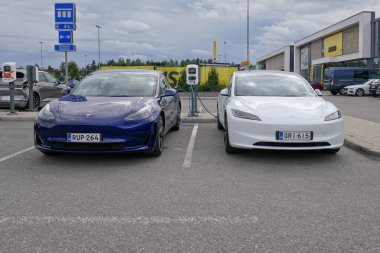 Laajalahti, Finlandiya - 19 Ağustos. 2025: Beyaz ve mavi Tesla Model 3 elektrikli araba alışveriş merkezinin park yerine park edildi elektrik şarj istasyonu.