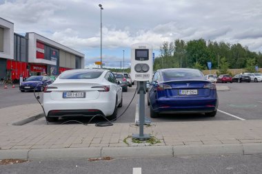 Laajalahti, Finlandiya - 19 Ağustos. 2025: Beyaz ve mavi Tesla Model 3 elektrikli araba alışveriş merkezinin park yerine park edildi elektrik şarj istasyonu.