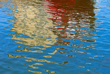 Abstract photograph focusing on the colorful reflections of a boat on rippling blue water in summer, Kruunuhaka, Helsinki, Finland.