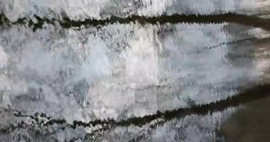 Bahar aylarında hafif dalgalı su yüzeyinde çıplak ağaçların ve açık gökyüzünün soyut yansımaları, Mustavuori, Helsinki, Finlandiya.