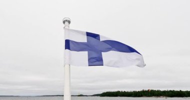 Finlandiya ulusal bayrağı bulutlu yaz havasında feribotun arkasında dalgalanıyor, Pirttisaari, Finlandiya, Avrupa.