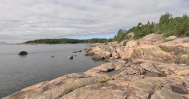 Pürüzsüz granit kayalık kıyıları ve güneşli yaz havasında yoğun bir kozalaklı orman hattının yer aldığı ada kıyıları, Pirttisaari, Finlandiya, Avrupa.