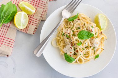 Linguine Pasta in White Sauce Garnished with Basil and Lemon on White Background, Italian Food Photography