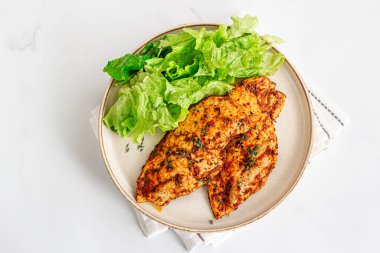 Yüksek proteinli fırın fırınlanmış tavuk göğsü. Tabakta taze marul var. Beyaz arka planda, fotoğrafın hemen üstünde.