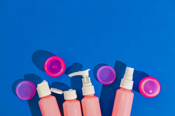 Cosmetic creams, lotion, spray for face in blank bottles on blue background. Flat lay, top view. Minimal beauty and spa concept. Empty space.