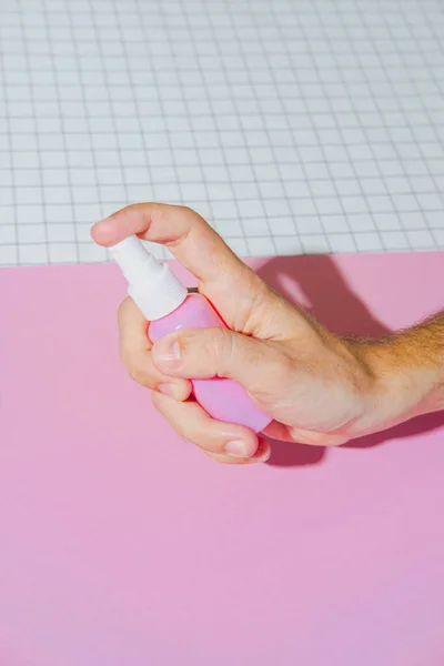 Cosmetic spray blank bottle in hand. Bio organic product on geometric pink and white background. minimal beauty and spa concept.