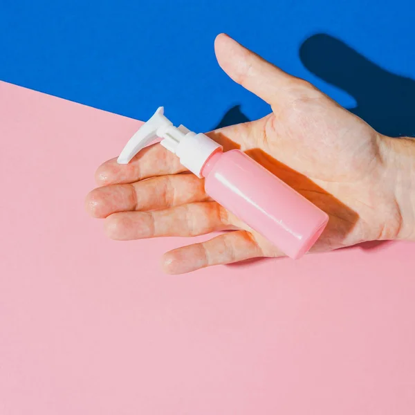 Cosmetic cream blank bottle in hand. Bio organic product on geometric pink and blue background. Minimal pop art concept